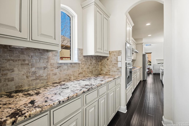 kitchen featuring light stone counters, backsplash, dark wood-style floors, stainless steel appliances, and arched walkways