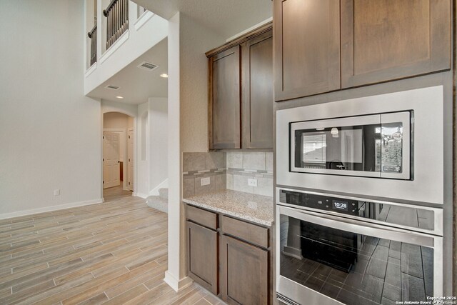 kitchen featuring light stone counters, visible vents, wood finish floors, decorative backsplash, and appliances with stainless steel finishes