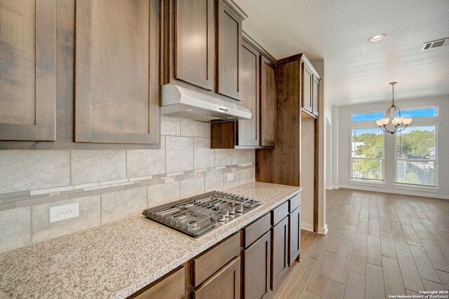 kitchen featuring visible vents, decorative backsplash, stainless steel gas stovetop, light wood-style floors, and under cabinet range hood