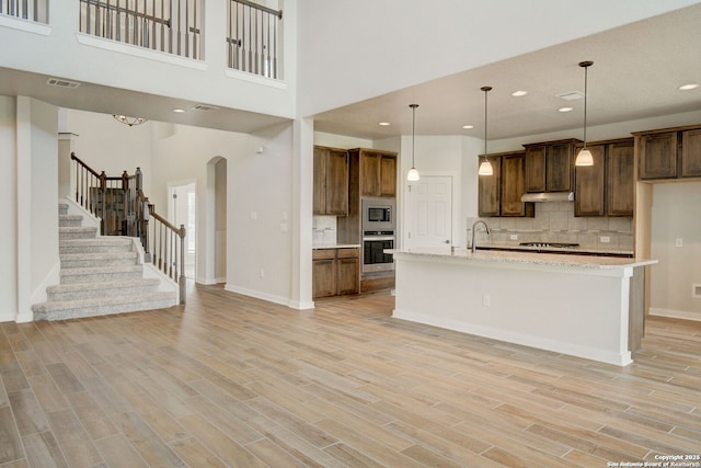 kitchen with visible vents, under cabinet range hood, appliances with stainless steel finishes, light wood finished floors, and decorative backsplash