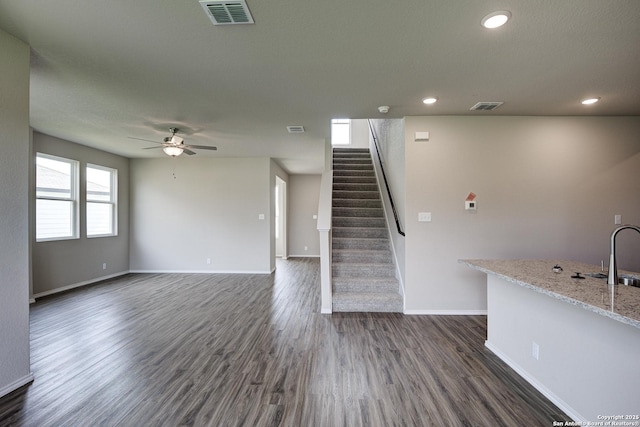 unfurnished living room with visible vents, dark wood-style floors, baseboards, ceiling fan, and stairs