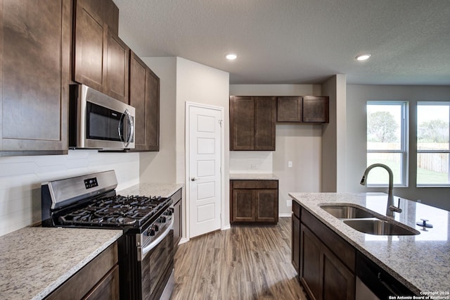 kitchen featuring wood finished floors, light stone countertops, a sink, stainless steel appliances, and dark brown cabinetry