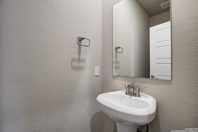 bathroom with a sink, visible vents, and a textured wall