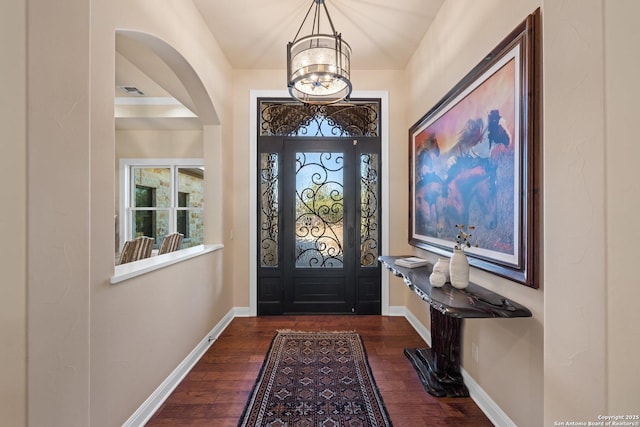 entrance foyer with a notable chandelier, dark wood-style floors, baseboards, and arched walkways