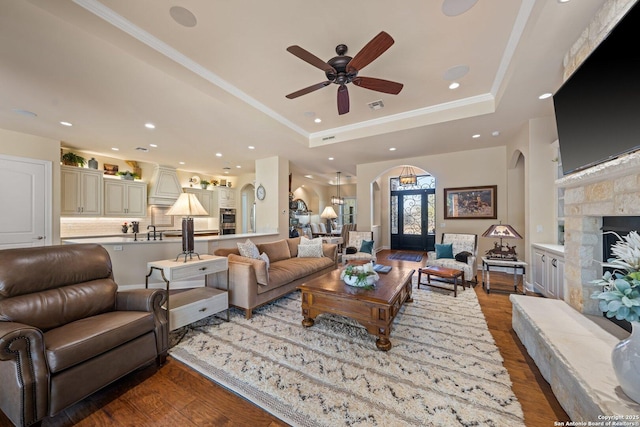 living room with wood finished floors, visible vents, a tray ceiling, a fireplace, and arched walkways