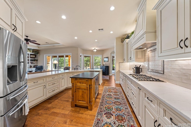 kitchen featuring open floor plan, recessed lighting, appliances with stainless steel finishes, light wood finished floors, and a raised ceiling