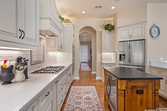 kitchen with tasteful backsplash, visible vents, a kitchen island, appliances with stainless steel finishes, and arched walkways