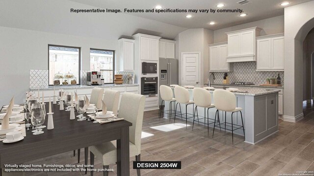 kitchen featuring backsplash, a breakfast bar area, stainless steel appliances, wood finished floors, and white cabinetry