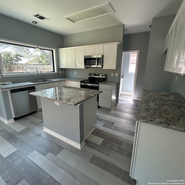 kitchen featuring visible vents, a sink, stainless steel appliances, white cabinets, and light stone countertops