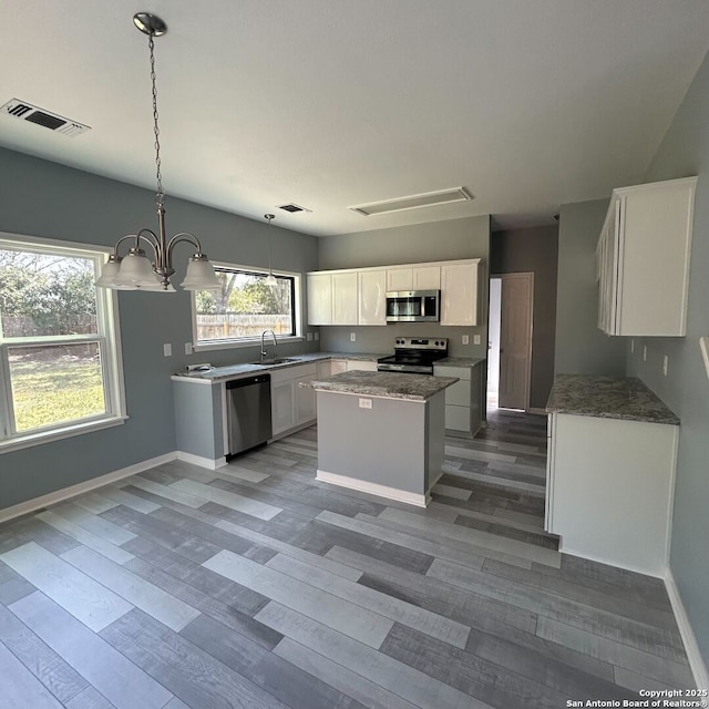 kitchen featuring visible vents, a kitchen island, appliances with stainless steel finishes, white cabinets, and a sink