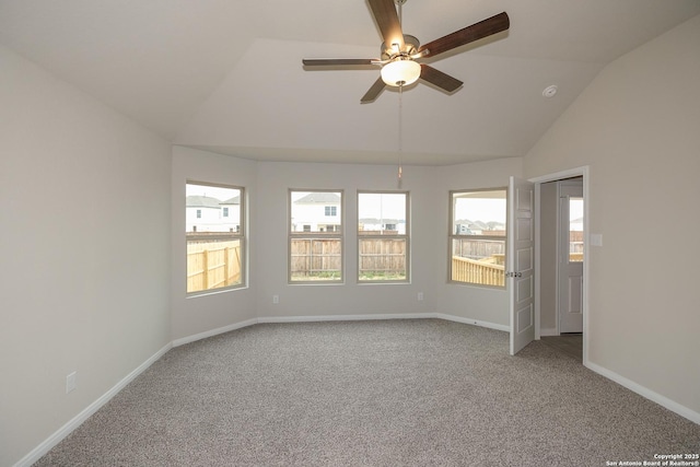 carpeted empty room featuring lofted ceiling, plenty of natural light, a ceiling fan, and baseboards