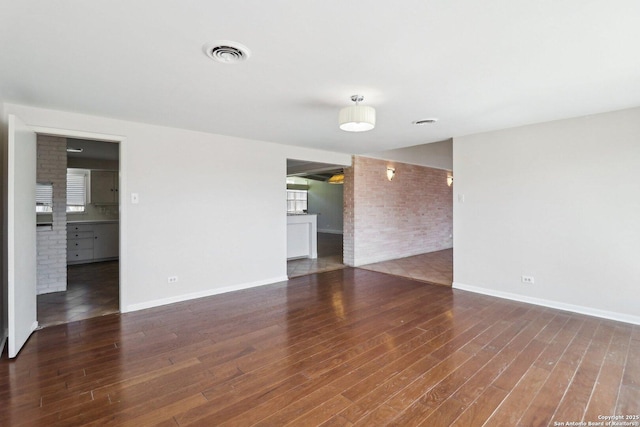 empty room featuring visible vents, brick wall, baseboards, and wood finished floors