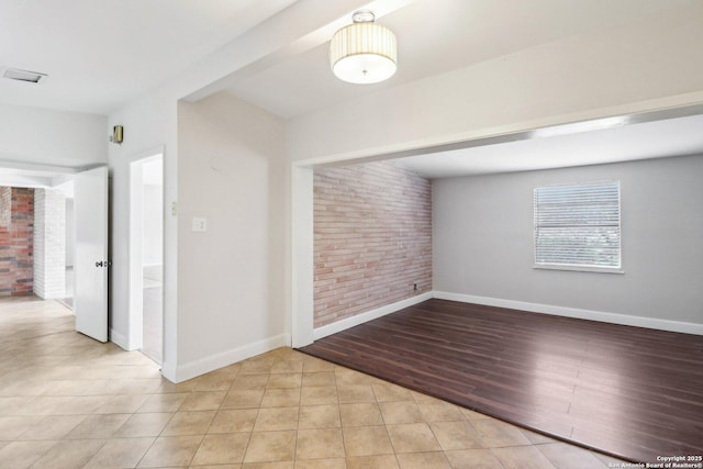 spare room with wood finished floors, baseboards, and brick wall