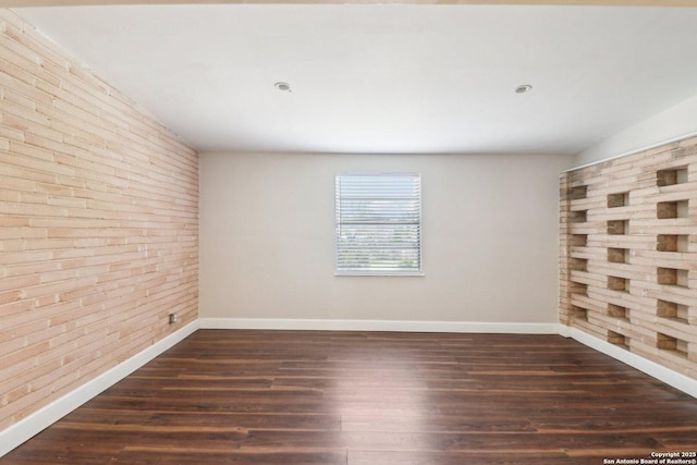 spare room featuring baseboards, dark wood-style flooring, and brick wall