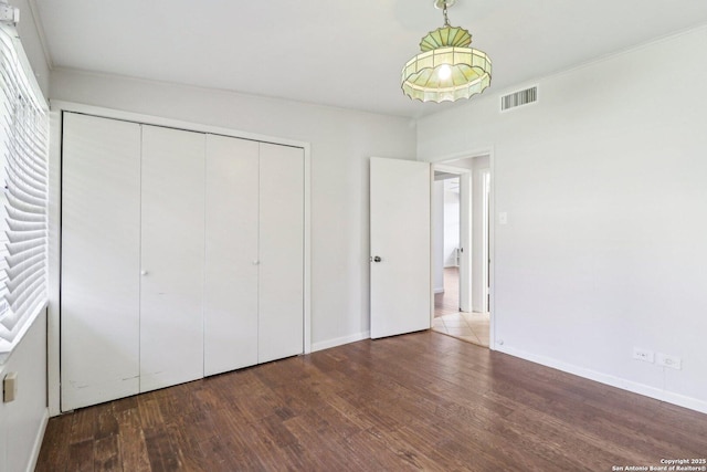 unfurnished bedroom featuring visible vents, baseboards, a closet, and wood finished floors