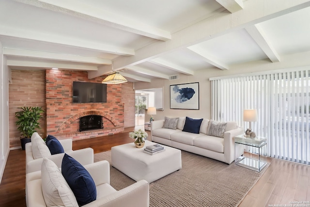 living room with visible vents, beam ceiling, a brick fireplace, and wood finished floors