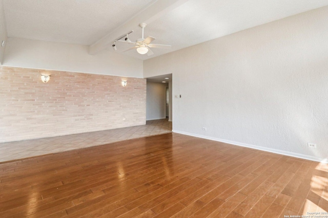 empty room with brick wall, vaulted ceiling with beams, baseboards, wood finished floors, and a ceiling fan