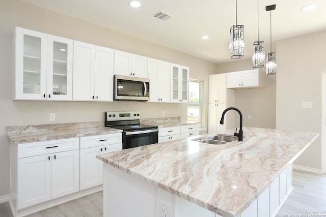 kitchen featuring white cabinets, a sink, a center island with sink, light stone counters, and stainless steel appliances