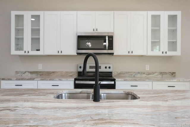 kitchen with white cabinetry, glass insert cabinets, appliances with stainless steel finishes, and light stone countertops