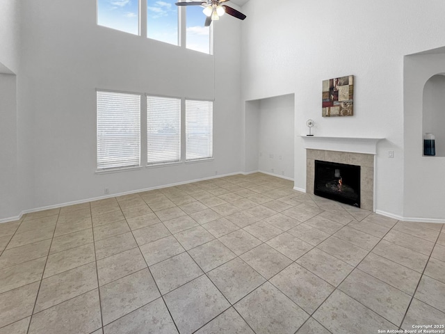 unfurnished living room with baseboards, a high ceiling, ceiling fan, a tiled fireplace, and tile patterned floors