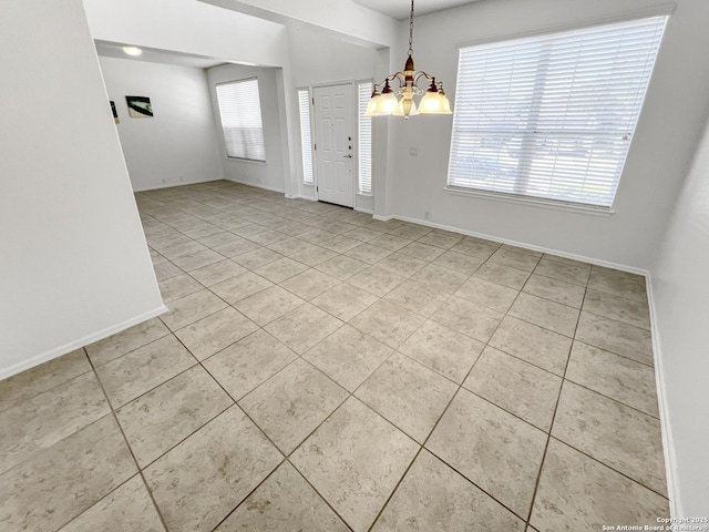 tiled spare room with baseboards, plenty of natural light, and a notable chandelier