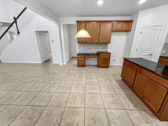 kitchen featuring light tile patterned floors, built in desk, dark countertops, brown cabinets, and backsplash