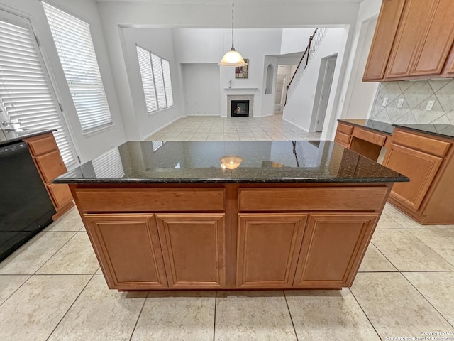 kitchen featuring tasteful backsplash, a glass covered fireplace, dark stone counters, brown cabinetry, and dishwasher