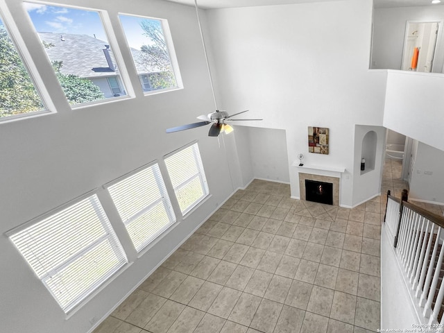 living area with a towering ceiling, ceiling fan, a tiled fireplace, and light tile patterned floors