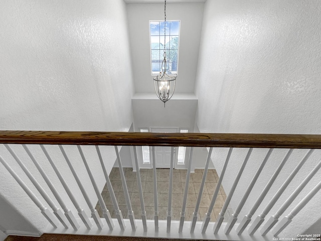 stairs featuring an inviting chandelier and a textured wall