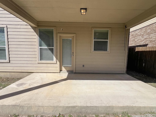 view of exterior entry with a patio area and fence