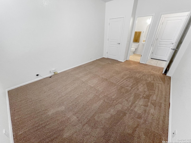 unfurnished bedroom with tile patterned floors, baseboards, ensuite bathroom, and carpet flooring