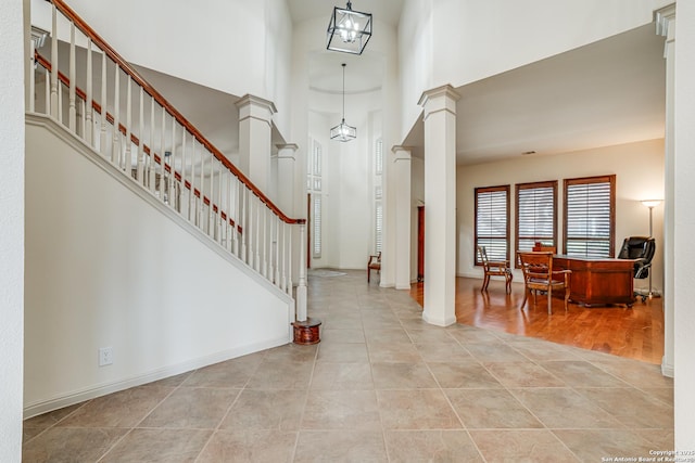 entrance foyer featuring baseboards, ornate columns, stairs, a towering ceiling, and tile patterned floors