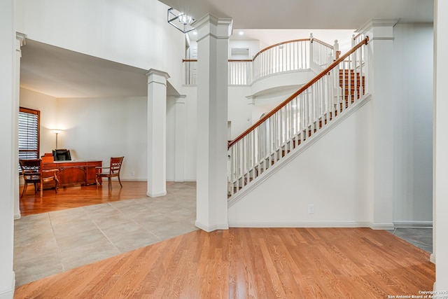 staircase featuring baseboards, wood finished floors, a towering ceiling, and decorative columns