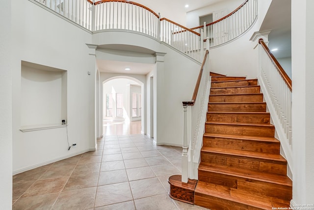 stairway with arched walkways, tile patterned floors, baseboards, and a towering ceiling