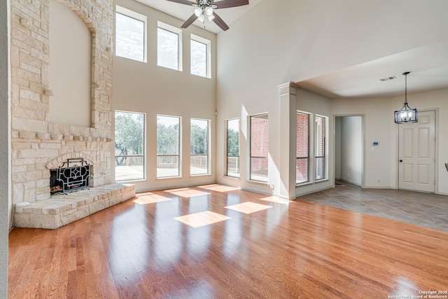 unfurnished living room featuring a stone fireplace, wood finished floors, baseboards, and ceiling fan