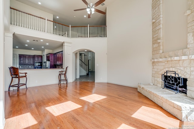 living room featuring ceiling fan, stairs, a stone fireplace, light wood-style flooring, and arched walkways