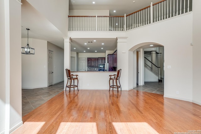 kitchen with a breakfast bar, light wood-style flooring, arched walkways, a peninsula, and ornate columns