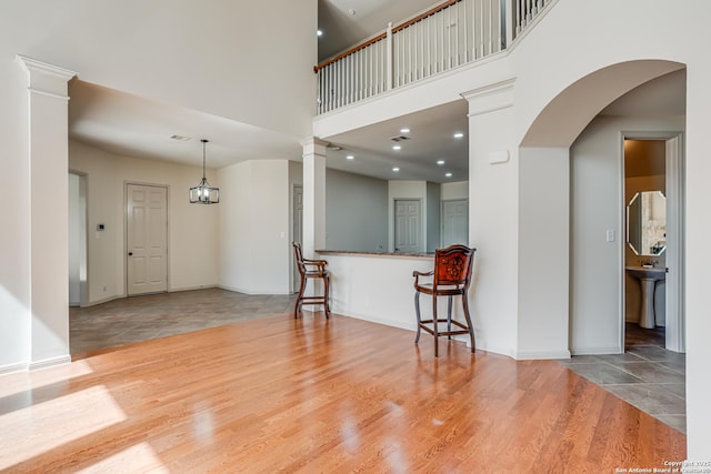 living area featuring decorative columns, wood finished floors, baseboards, and a towering ceiling