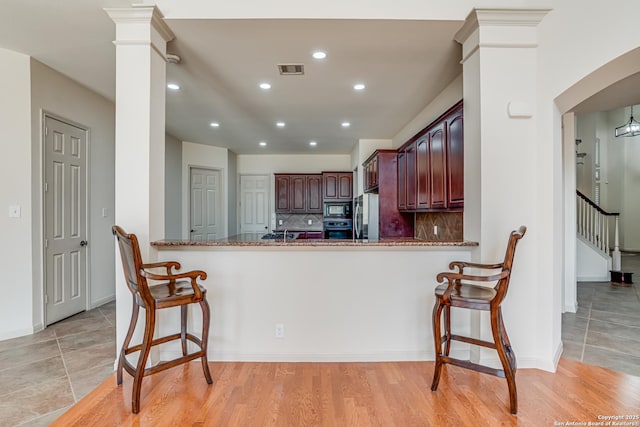 kitchen with visible vents, decorative columns, freestanding refrigerator, black microwave, and decorative backsplash