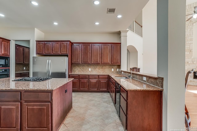 kitchen featuring light stone countertops, visible vents, a sink, decorative backsplash, and black appliances