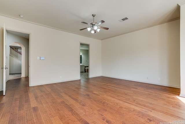 unfurnished room featuring wood finished floors, arched walkways, visible vents, and ornamental molding