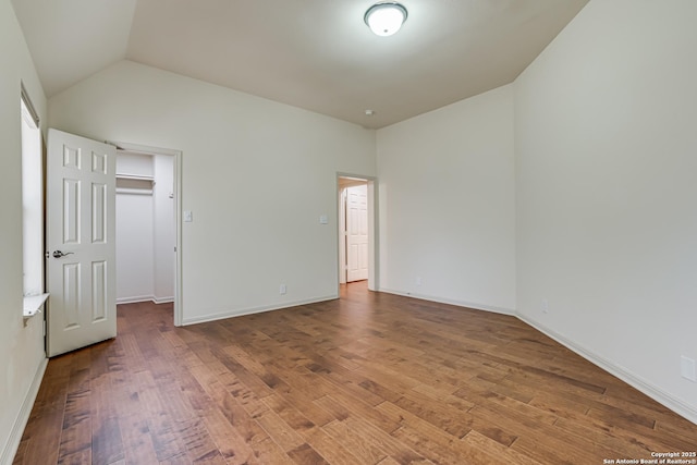 unfurnished bedroom with a walk in closet, baseboards, hardwood / wood-style floors, and vaulted ceiling