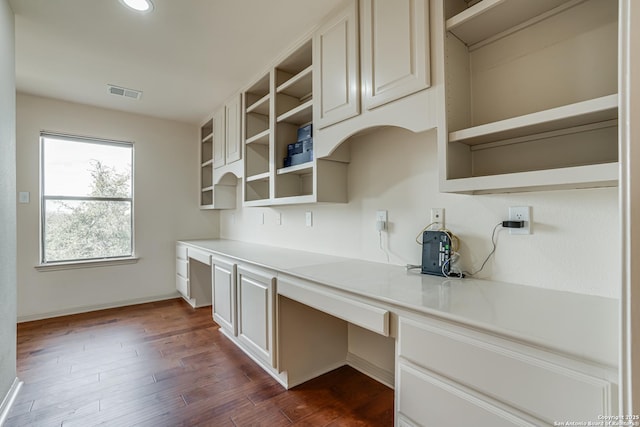 unfurnished office featuring visible vents, baseboards, dark wood-style floors, and built in desk