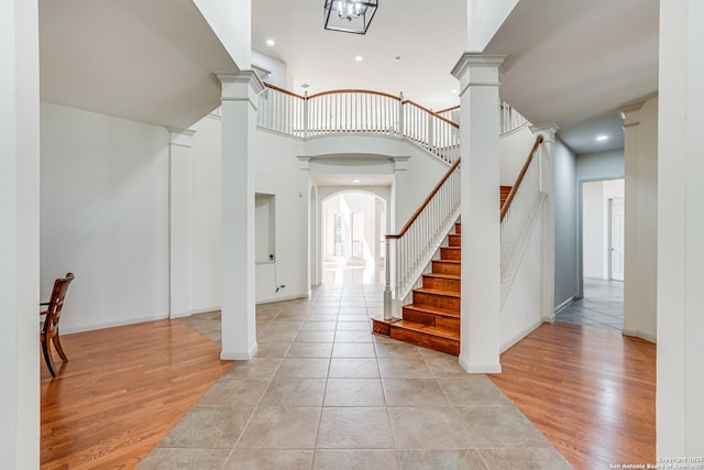 entryway featuring decorative columns, arched walkways, light wood-style flooring, and stairs