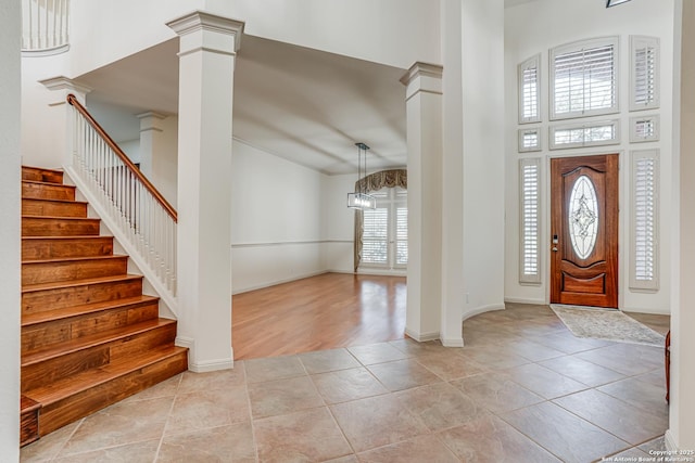 entrance foyer featuring stairway, light tile patterned floors, baseboards, ornate columns, and a towering ceiling