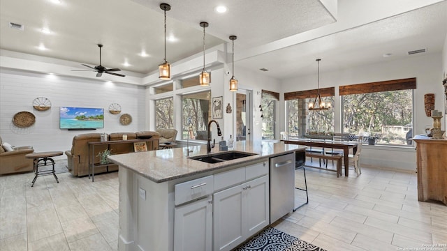 kitchen with light stone counters, visible vents, a sink, stainless steel dishwasher, and open floor plan