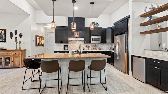 kitchen featuring a breakfast bar area, light stone counters, dark cabinets, appliances with stainless steel finishes, and tasteful backsplash