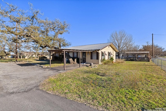 exterior space featuring driveway, a front lawn, fence, metal roof, and a carport