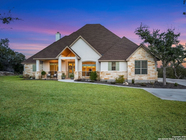 view of front of property featuring stone siding, a porch, a yard, a shingled roof, and a chimney