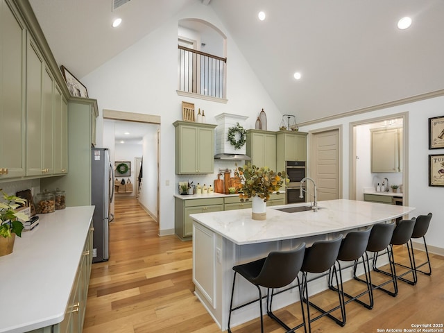 kitchen featuring a breakfast bar, a sink, stainless steel appliances, light wood-style floors, and green cabinetry